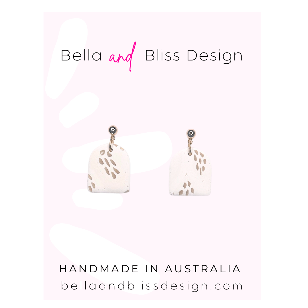 White earrings with black speckles on a pink and white gradient background with 'Bella and Bliss Design' branding.