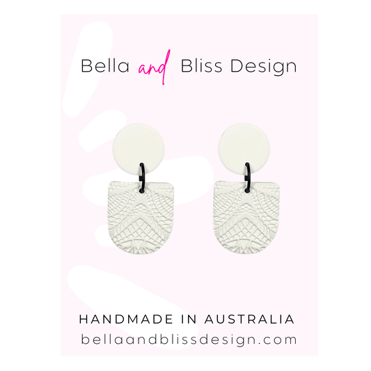 White earrings with textured design on a light pink background, featuring Bella and Bliss Design branding.
