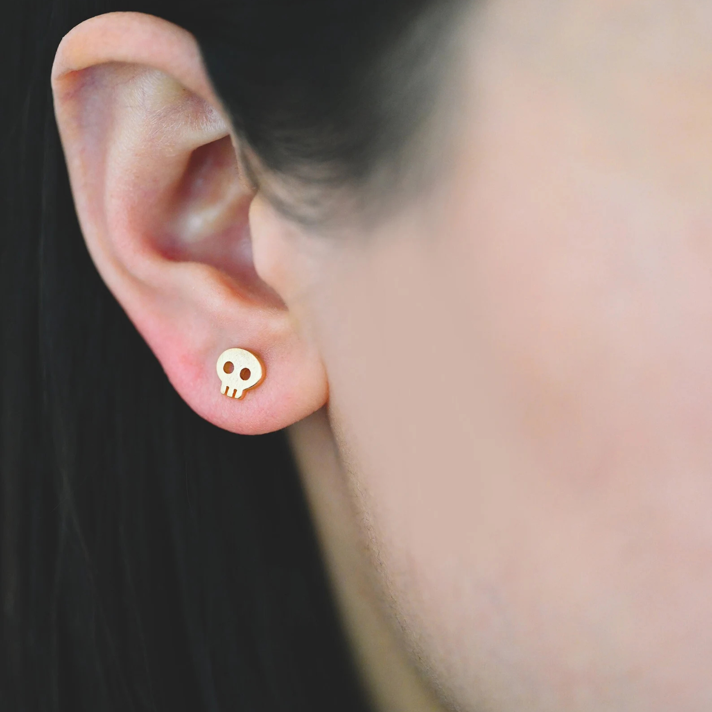 Gold skull-shaped earring worn on an ear with a blurred background