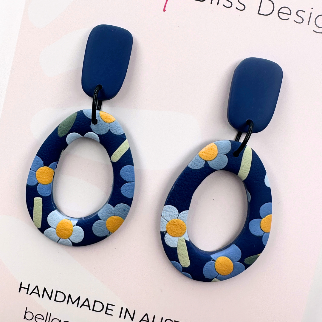 Blue floral earrings with 'Bella and Bliss Design' branding on a pink background