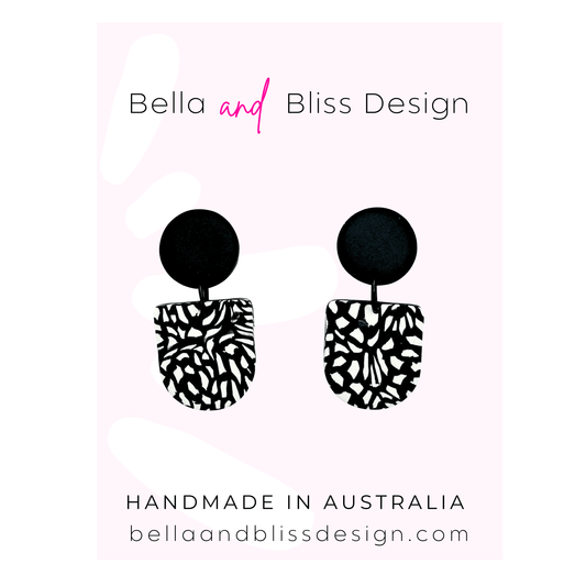 Black and white patterned earrings with 'Bella and Bliss Design' branding on a light pink background.