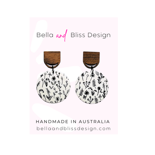 Wooden earrings with floral patterns on a light pink background, branded as Bella and Bliss Design.