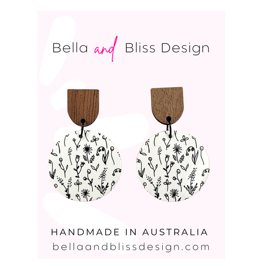 Wooden earrings with floral designs on a pink background, featuring Bella and Bliss Design branding.