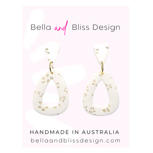 White teardrop earrings with gold accents on a pink background, featuring Bella and Bliss Design branding.