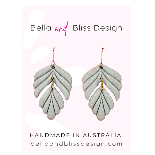 Leaf-shaped earrings with Bella and Bliss Design branding on a light pink background