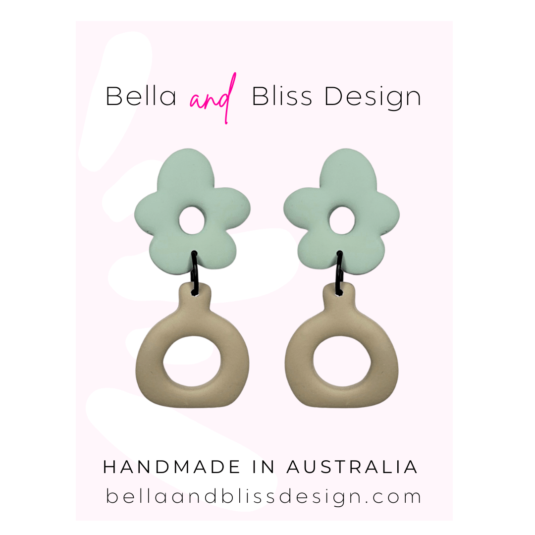Flower-shaped earrings with pink floral tops and beige circular bases on a light pink background, featuring 'Bella and Bliss Design'.