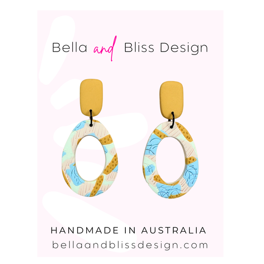 Colorful earrings with 'Bella and Bliss Design' branding on a light pink background.