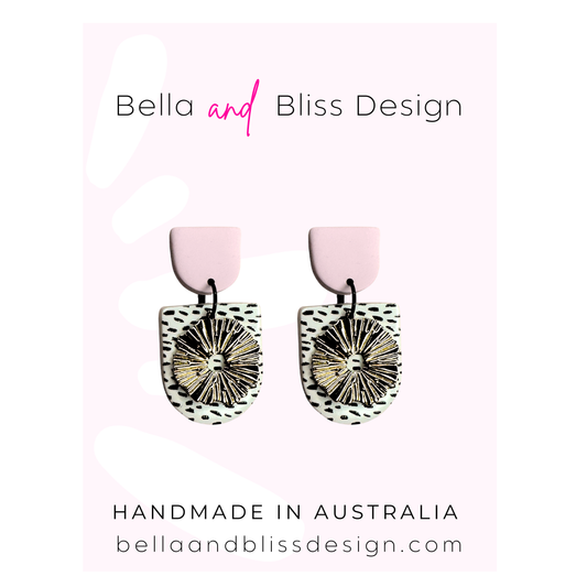 Earrings with pink tops and black and gold designs on a light pink background, featuring Bella and Bliss Design branding.