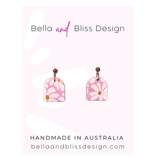 Pink floral earrings with 'Bella and Bliss Design' branding on a light pink background.