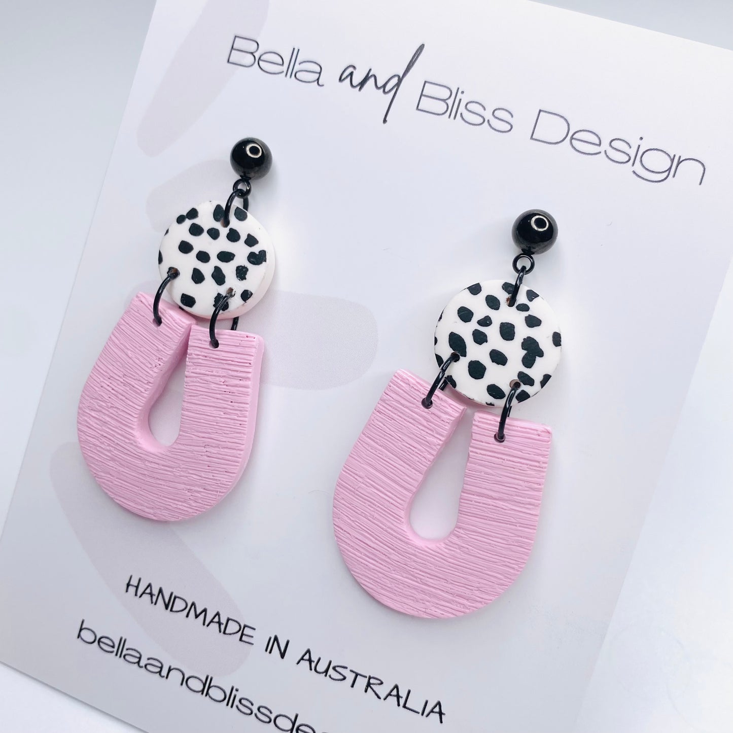 Pink earrings with black and white patterned tops on a light pink background, featuring Bella and Bliss Design branding.