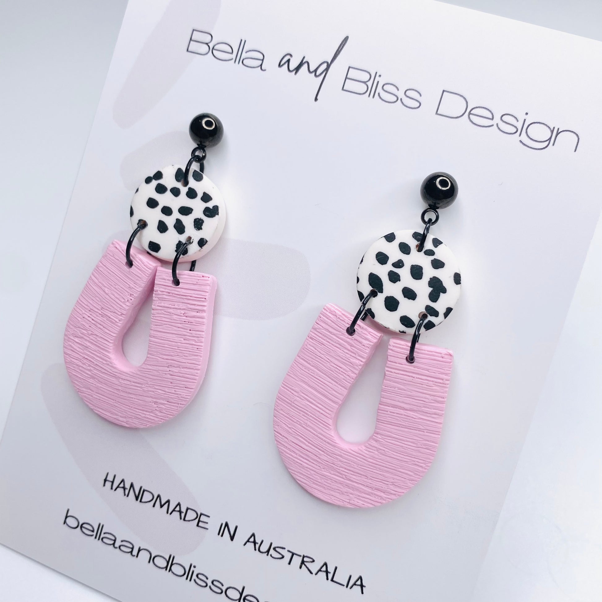 Pink earrings with black and white patterned tops on a light pink background, featuring Bella and Bliss Design branding.