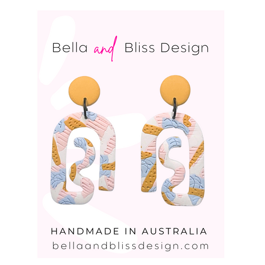 Colorful earrings with 'Bella and Bliss Design' branding on a pink background