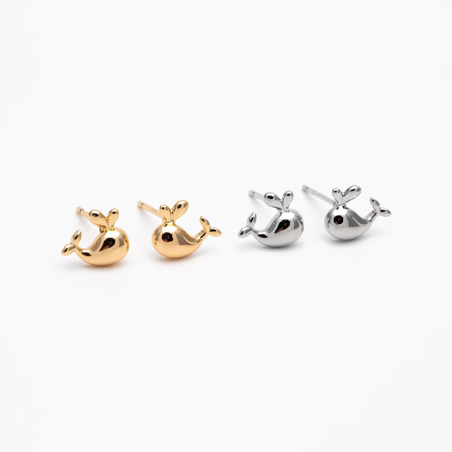 Pair of gold and silver whale-shaped earrings on a white background