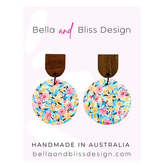 Floral earrings with wooden accents on a pink background, branded as Bella and Bliss Design.