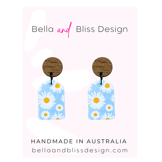 Pair of earrings with floral design on a pink background, featuring 'Bella and Bliss Design'.