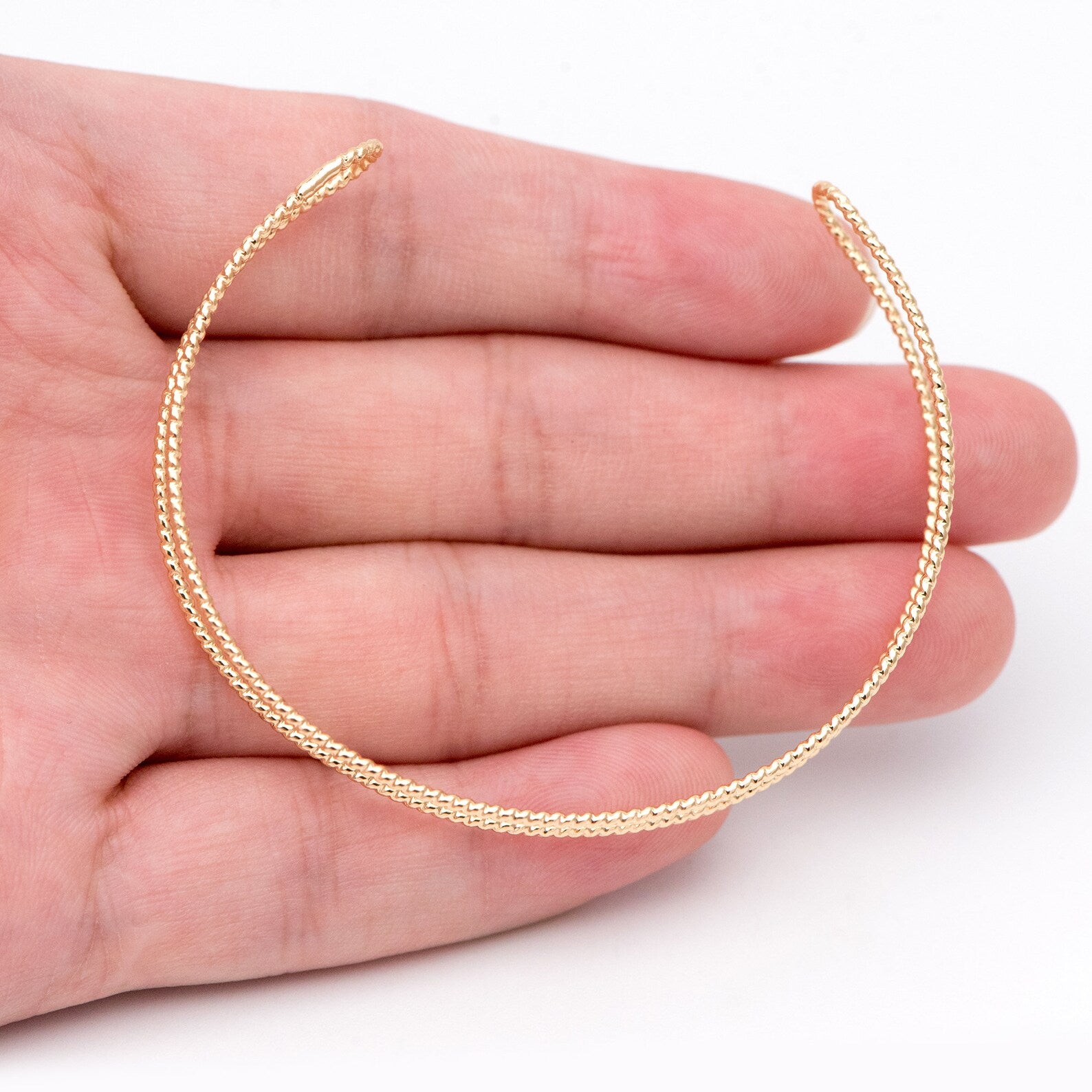 Gold chain necklace draped over a hand on a white background