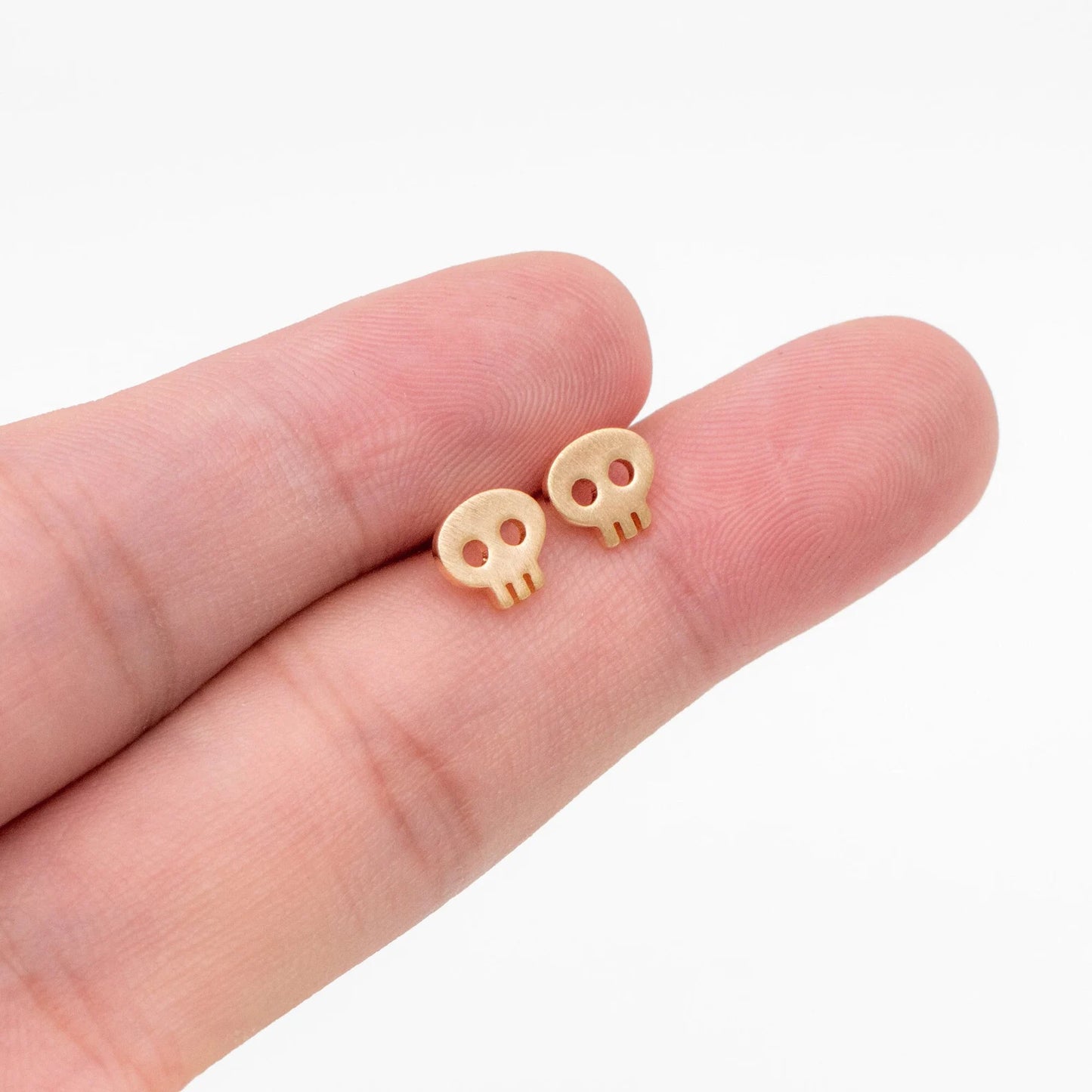 Small skull earrings held between fingers on a white background