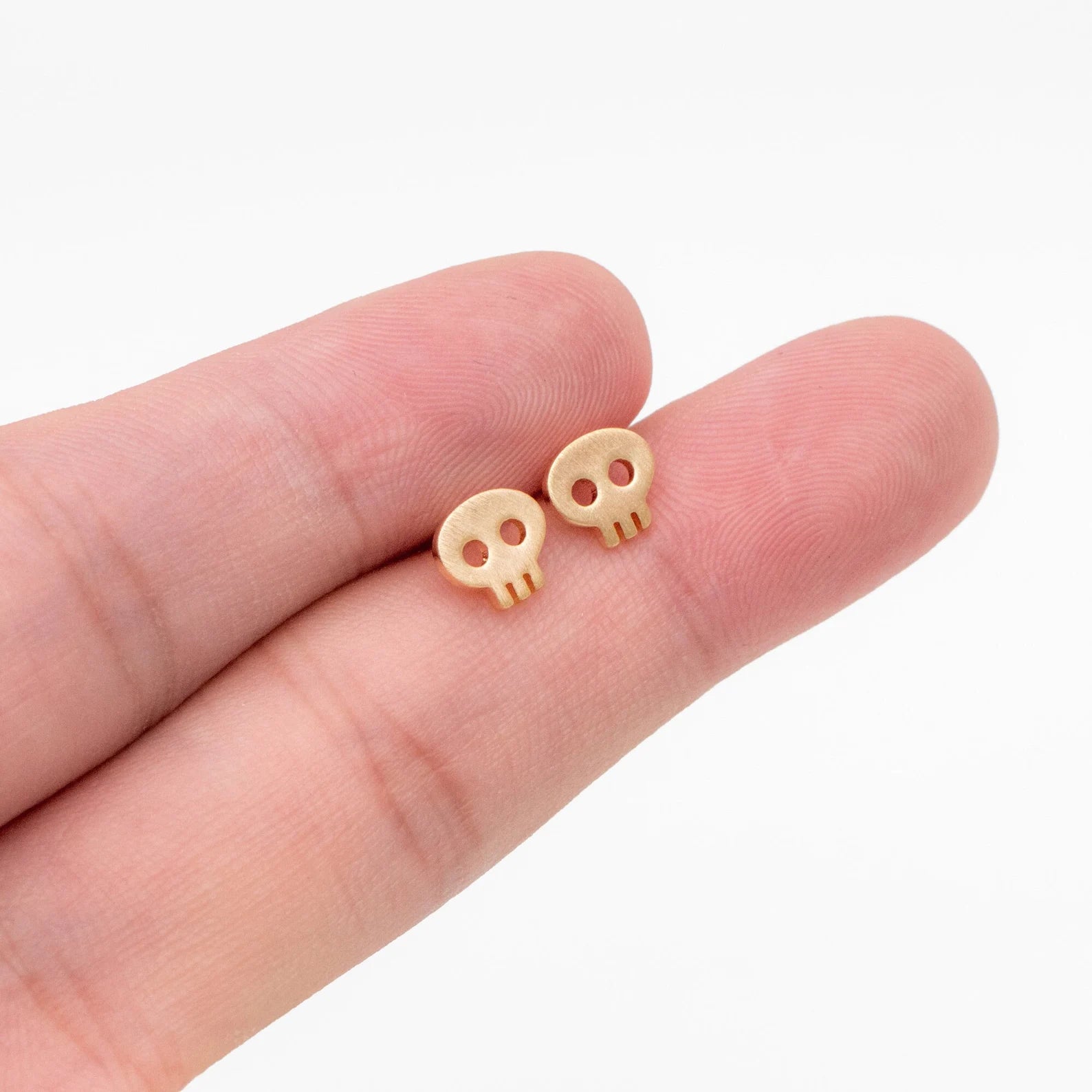 Small skull earrings held between fingers on a white background