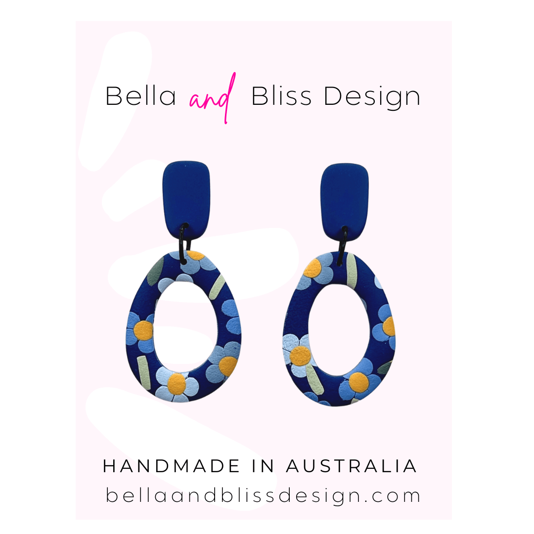 Blue floral earrings with 'Bella and Bliss Design' branding on a pink background
