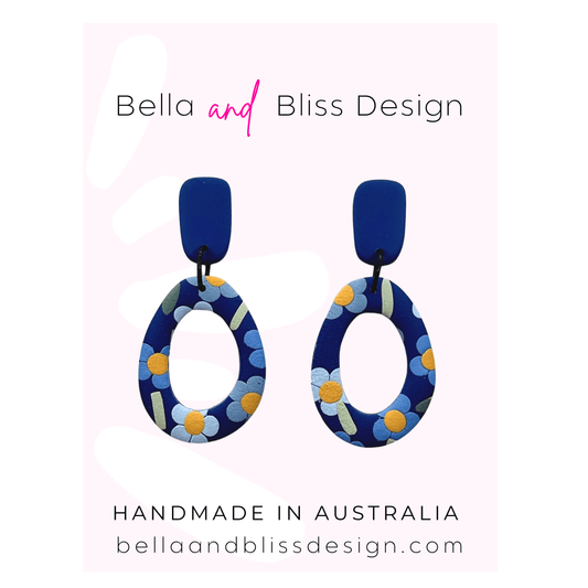 Blue floral earrings with 'Bella and Bliss Design' branding on a pink background