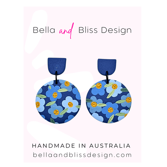 Blue floral earrings with 'Bella and Bliss Design' branding on a pink background