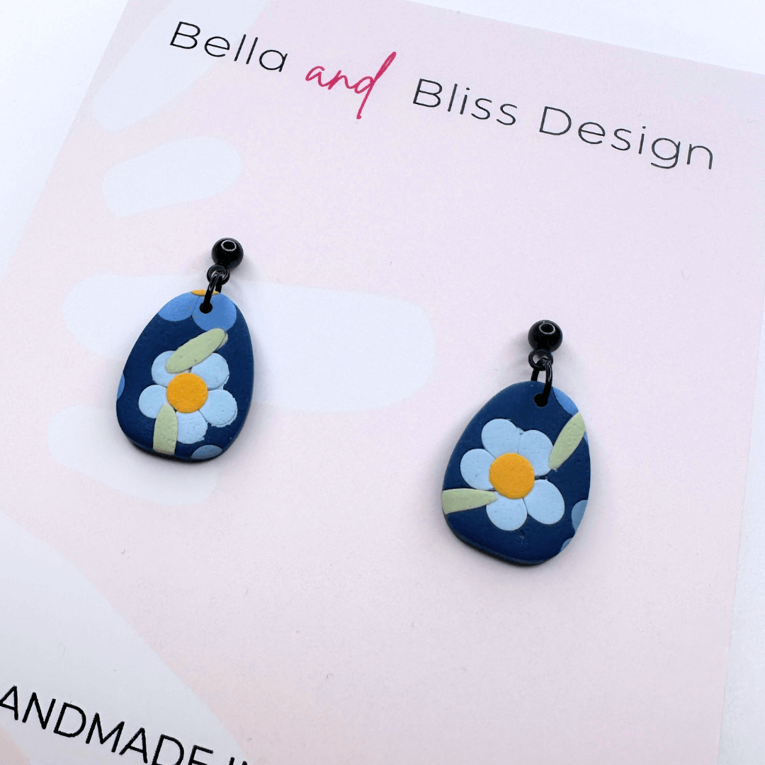 Blue floral earrings with 'Bella and Bliss Design' branding on a pink background