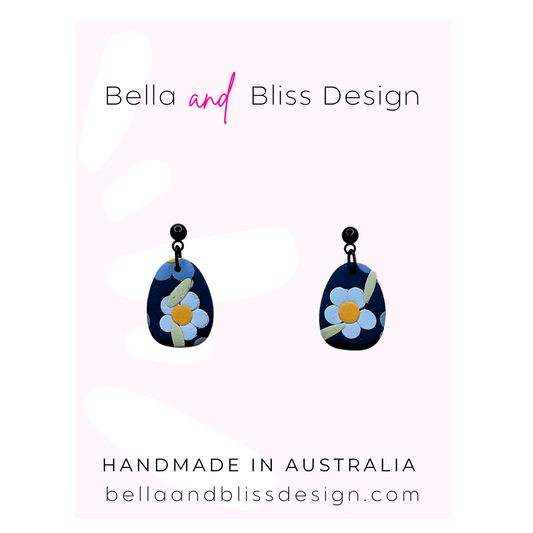 Blue floral earrings with 'Bella and Bliss Design' branding on a pink background