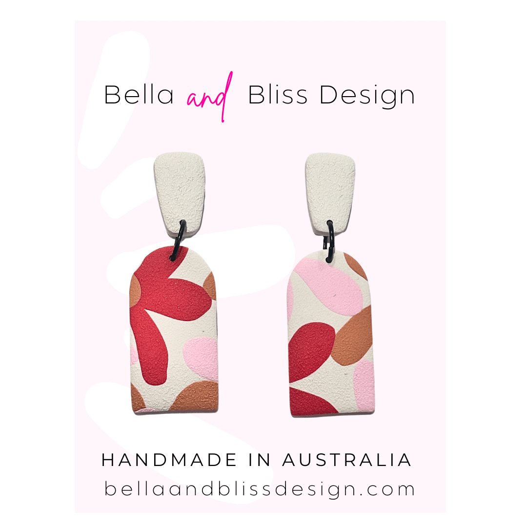 Pair of earrings with colorful design on a light pink background, featuring 'Bella and Bliss Design'.