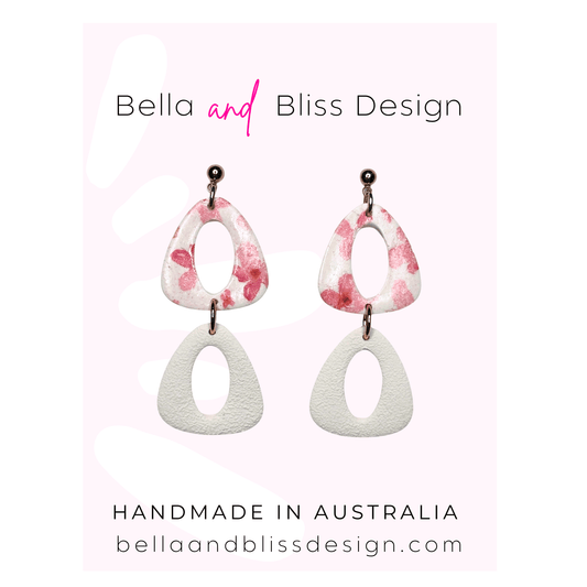 Pair of earrings with pink and white design on a light pink background, featuring 'Bella and Bliss Design'.
