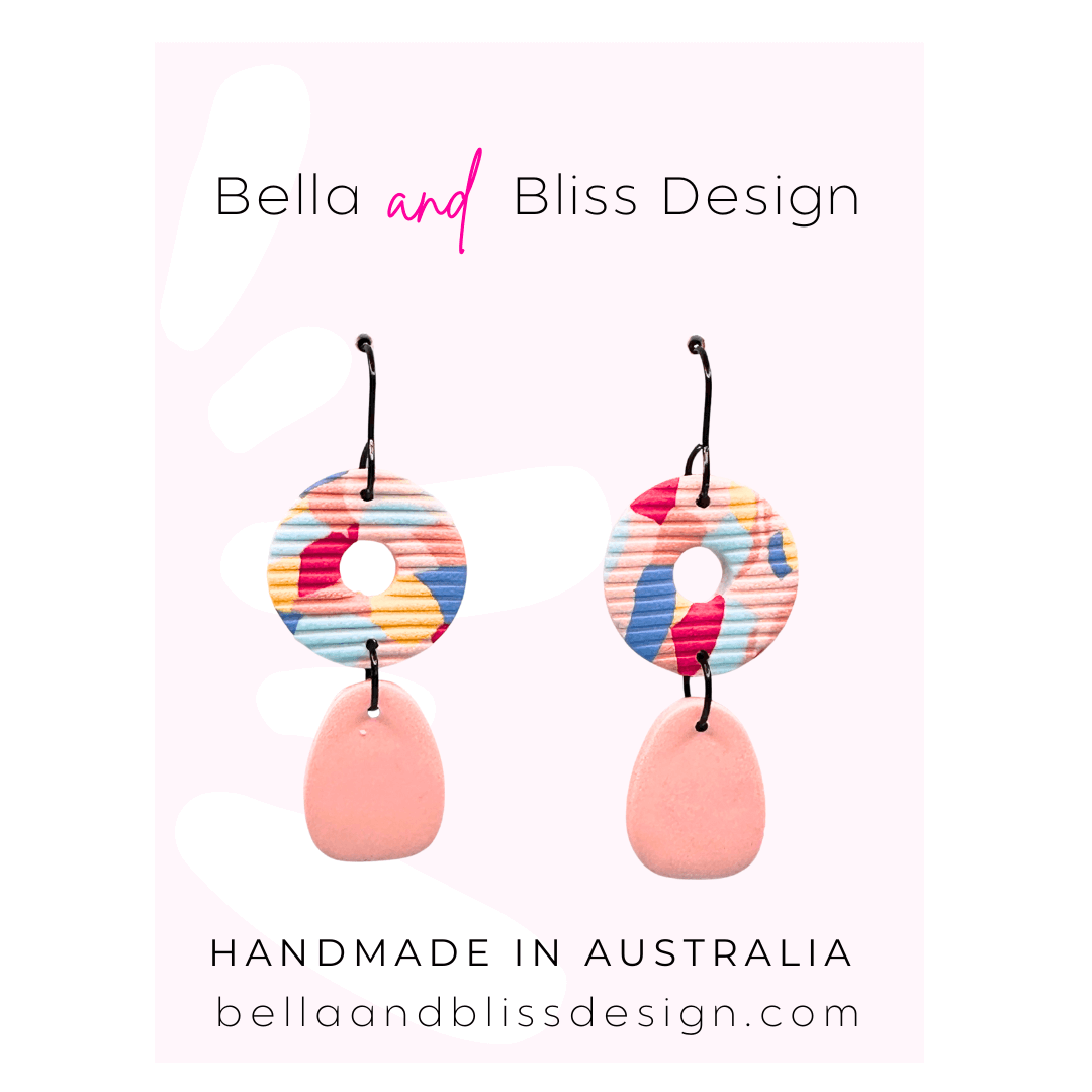 Colorful earrings with a pink base and multicolored circular top on a light pink background with 'Bella and Bliss Design' branding.