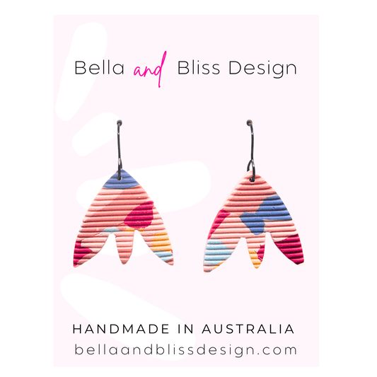 Colorful earrings with 'Bella and Bliss Design' branding on a pink background