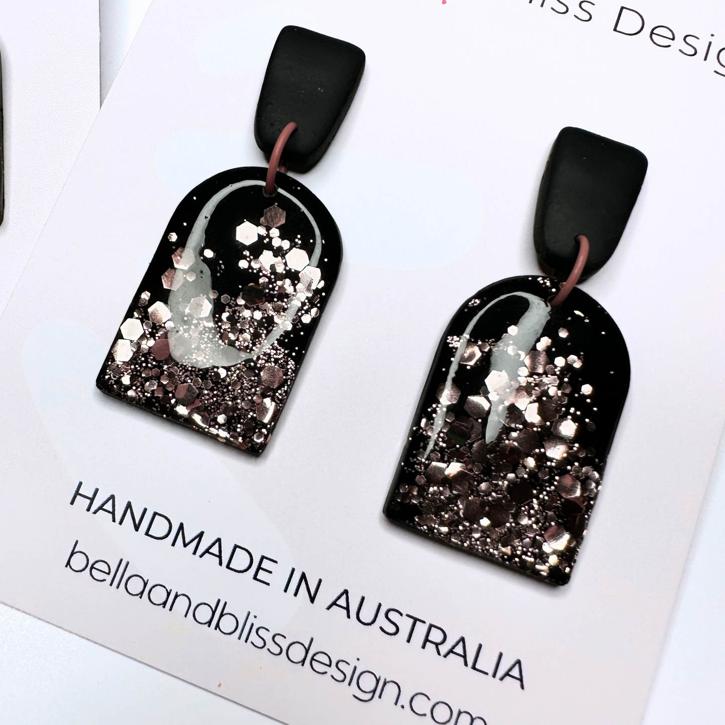 Black earrings with pink glitter  featuring Bella and Bliss Design branding.