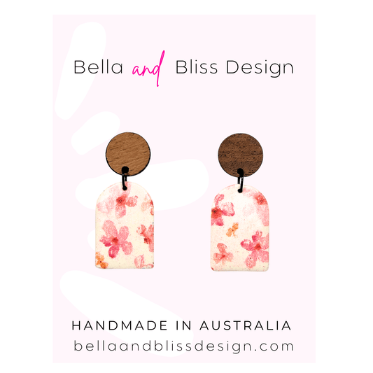 Pair of floral earrings with wooden backing on a pink background, branded 'Bella and Bliss Design'.