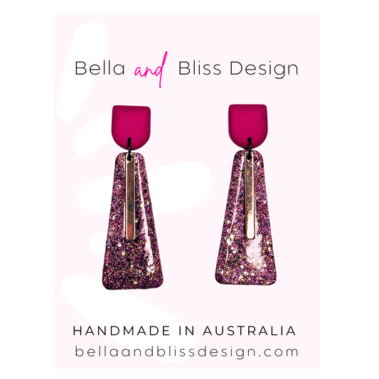 Pink glittery earrings with 'Bella and Bliss Design' branding on a light pink background.