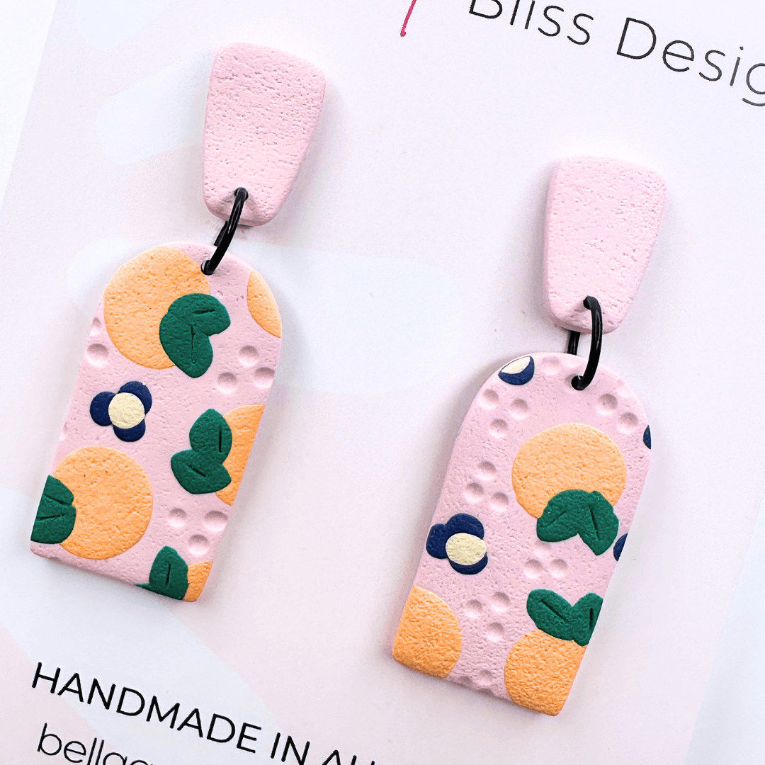 Peach Blossom Dangle Earrings with 'Bella and Bliss Design' branding on a pink background