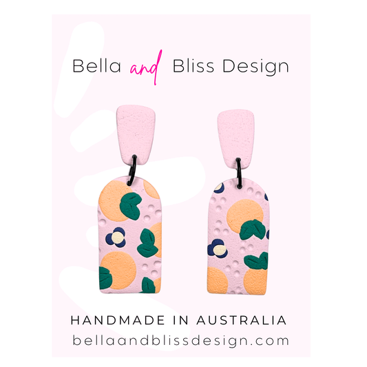 Peach Blossom Dangle Earrings with 'Bella and Bliss Design' branding on a pink background