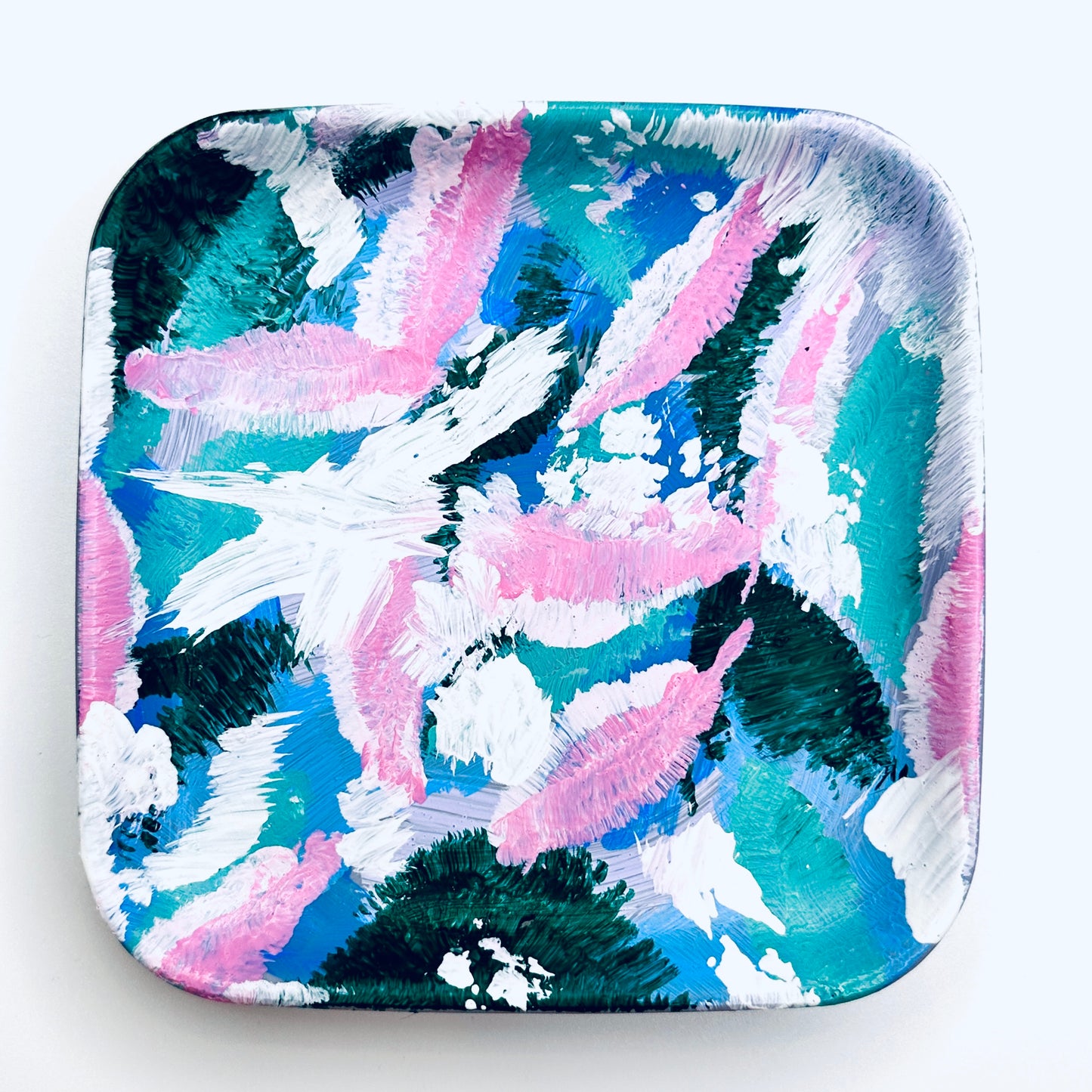 A hand-painted jewellery dish featuring a peacock pattern in green, brown, white, and pink colors on a white background.